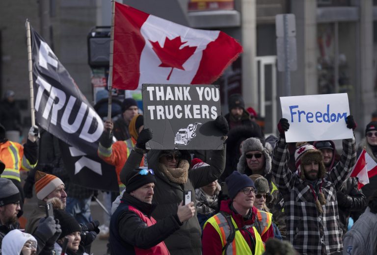 Protestujúci mávajú plagátmi a vlajkou počas demonštrácie v Ottawe. Foto: TASR/AP