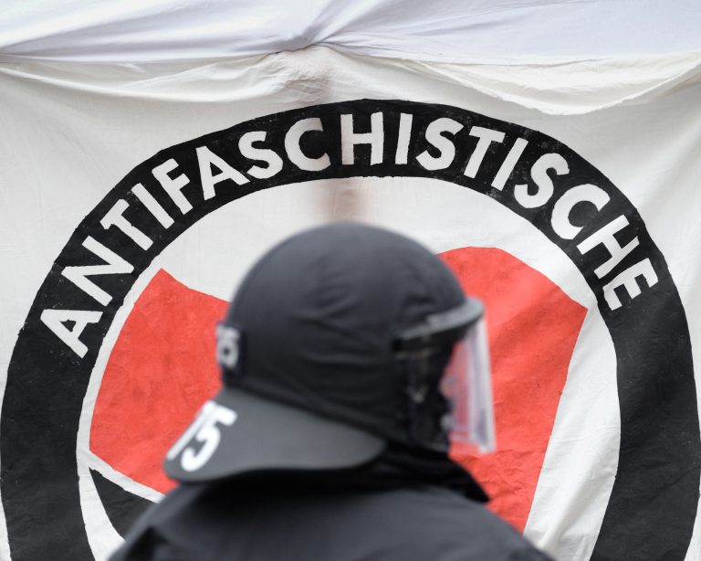 Ein Polizist steht vor einem Antifa-Transparent. Foto: Sebastian Willnow/picture alliance via Getty Images