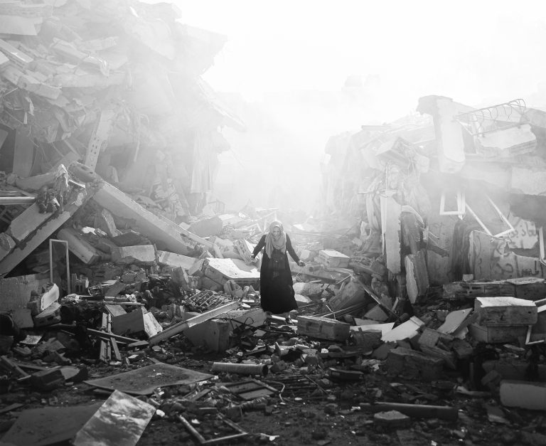 Rozrušená obyvateľka kráča pomedzi trosky obytných budov po izraelských náletoch v štvrti al-Zahra v Pásme Gazy. Foto: Mustafa Hassona/Anadolu via Getty Images 