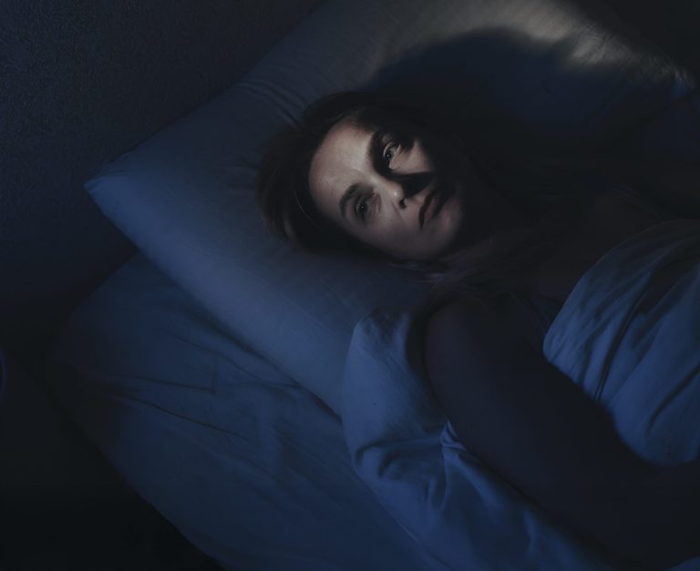A woman lies awake in bed, unable to fall asleep, a common experience in a 24/7 world. Photo: Ekaterina Goncharova / Getty Images