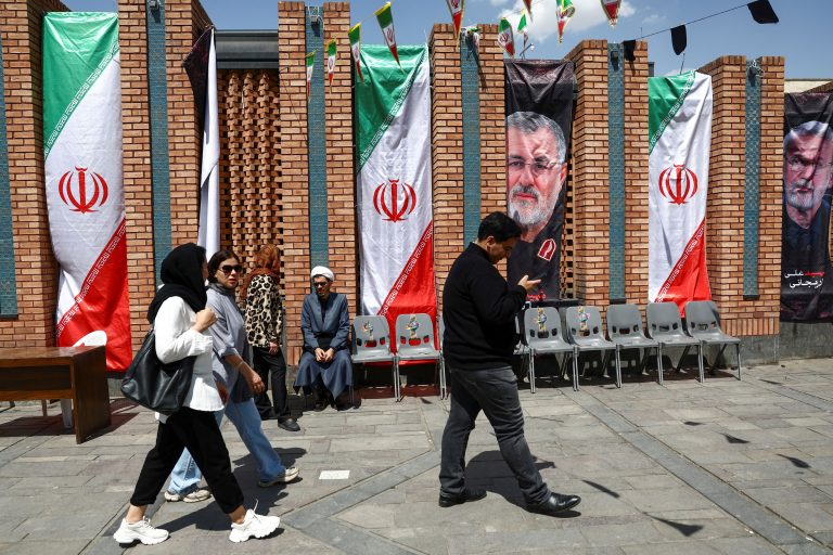 People walk past a banner with a picture of the IRGC.