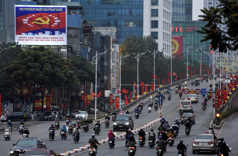 Autá a motocykle prechádzajú okolo bannerov Komunistickej strany Vietnamu.